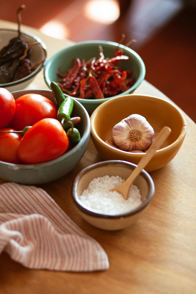 A vibrant display of fresh Mexican ingredients including tomatoes, chili peppers, garlic, and salt.